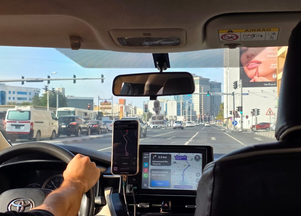View from inside a car showing a driver, mounted phone, and navigation screen in traffic