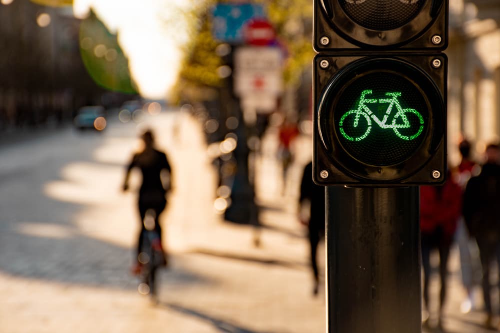 Person riding a green bicycle through an intersection while a traffic signal changes, illustrating urban cycling safety and traffic awareness.