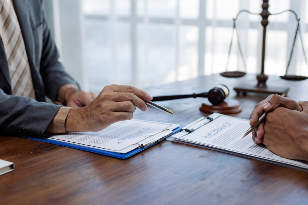 Two people reviewing insurance policy documents at a desk with a gavel and scales of justice